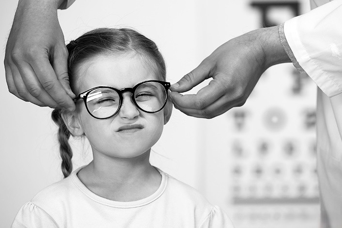 tay bác sĩ đang đeo kính cho một bé gái, ảnh trắng đen