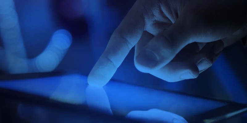 ngón tay đang ấn vào màn hình điện thoại phát ánh sáng xanh