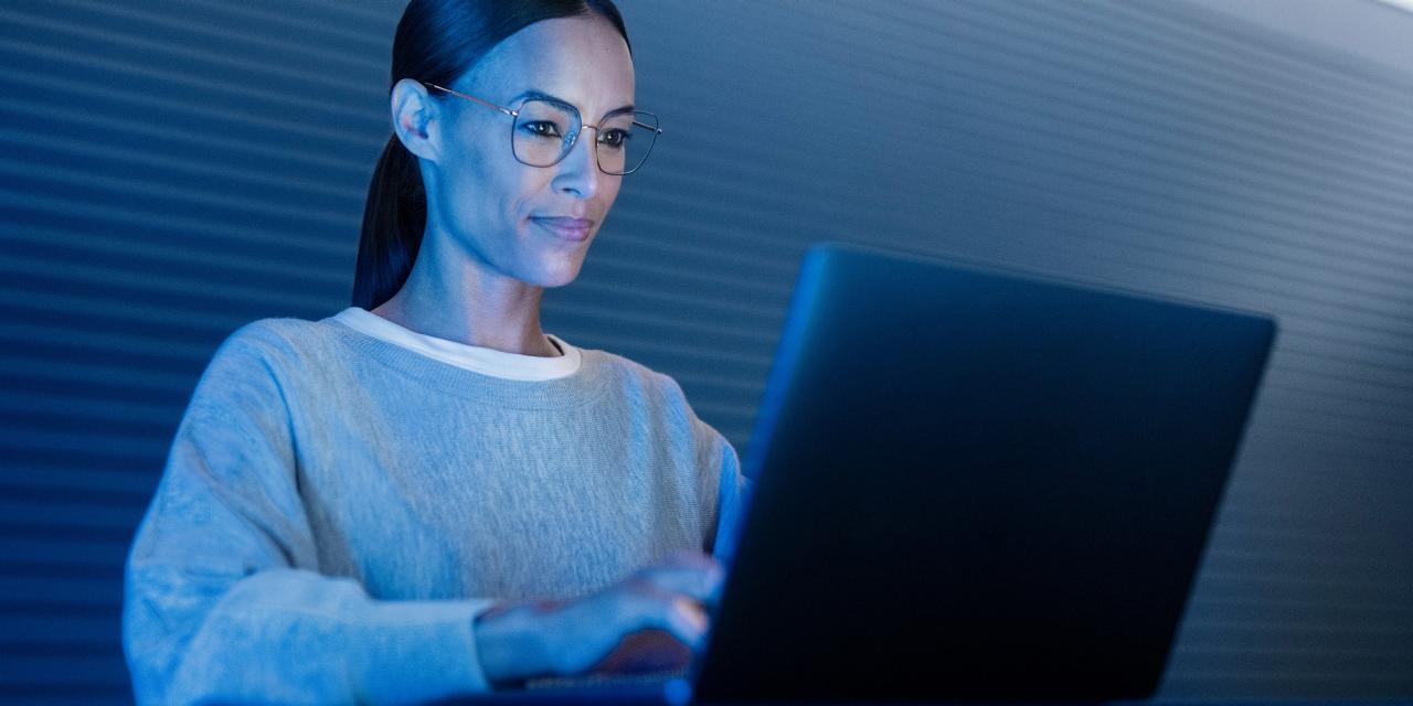 Người phụ nữ đeo kính Zeiss PhotoFusion X đang nhìn vào màn hình máy tính